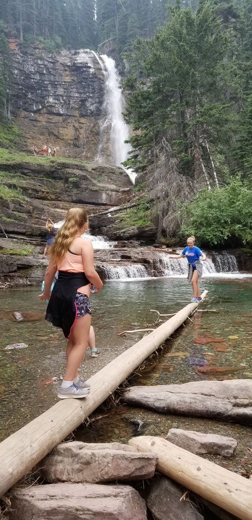 Two young girls walking along a downed tree resting in the water