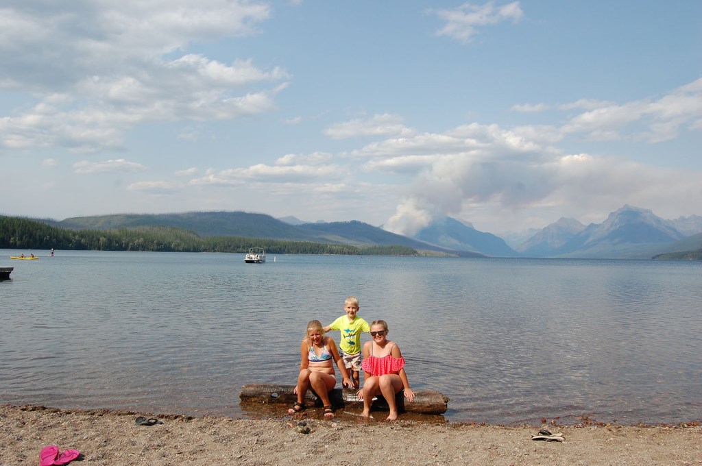 3 kids sitting on a log in a lake
