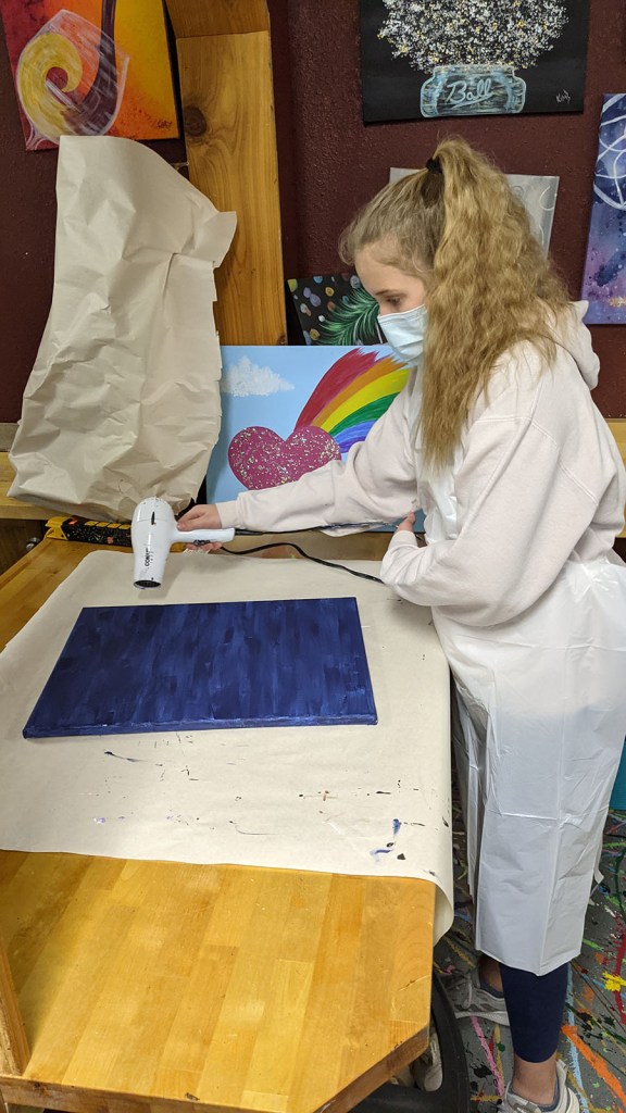 A young girl blow-drying a blue canvas