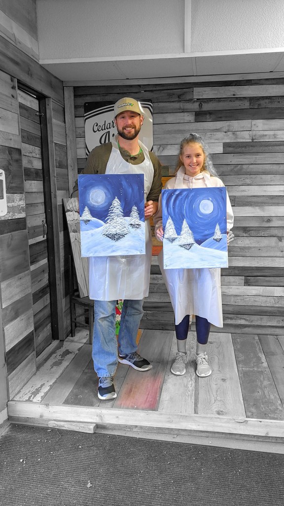 A father and daughter hold up their paintings