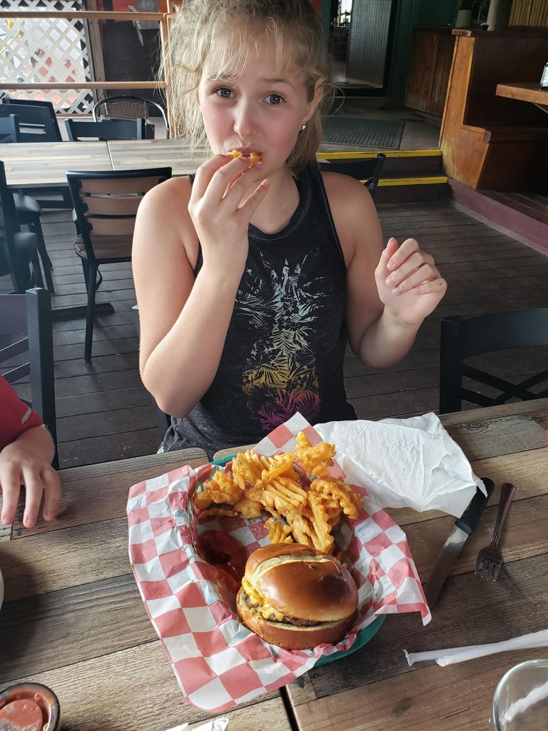 A young girl eating fries with a cheeseburger on the table