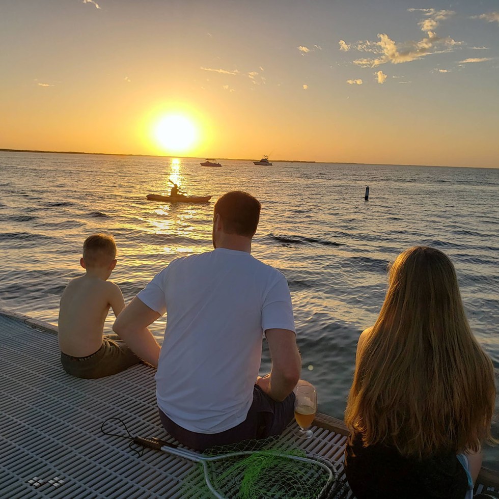 a family sitting on the dock at sunset