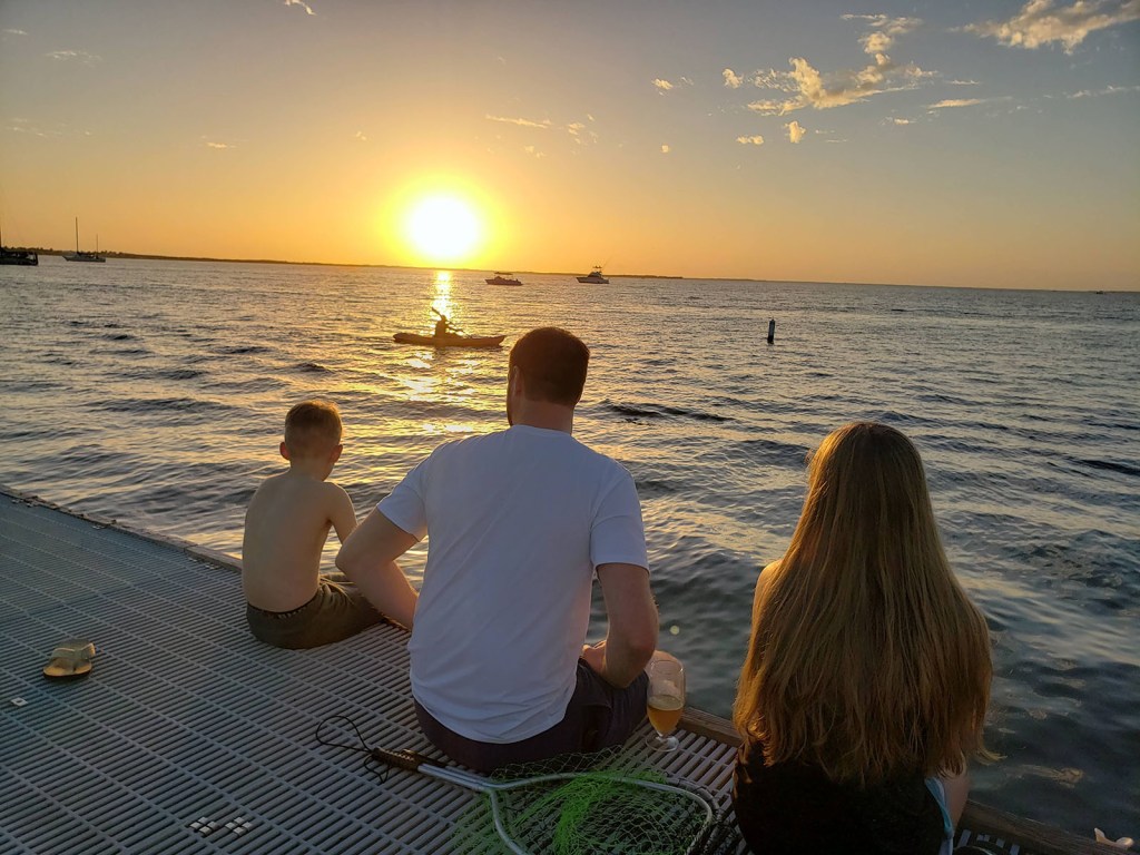 a family sitting on the dock at sunset