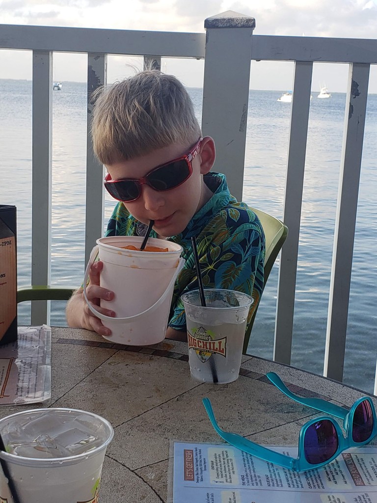 A boy in sunglasses drinking out of a bucket sized drink