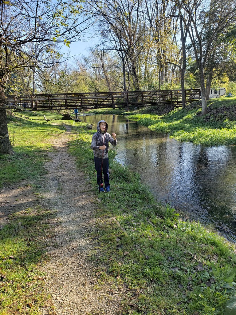 A boy fishing a stream next to a bridge