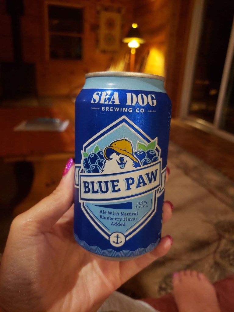 A woman with pink fingernails holds a blue Sea Dog beer can in a cabin