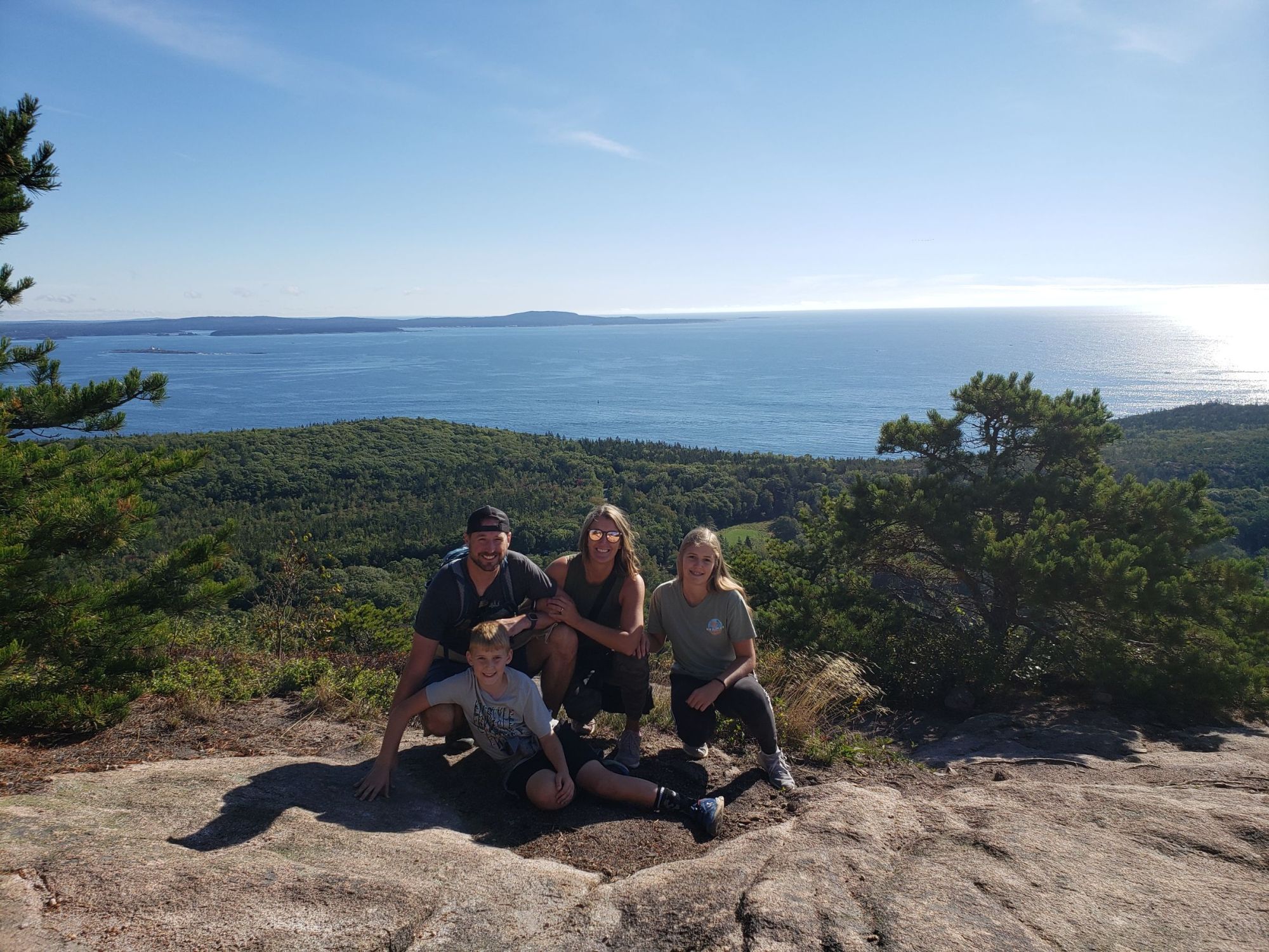 A family of 4 poses on a rock ground with the Atlantic Ocean behind them