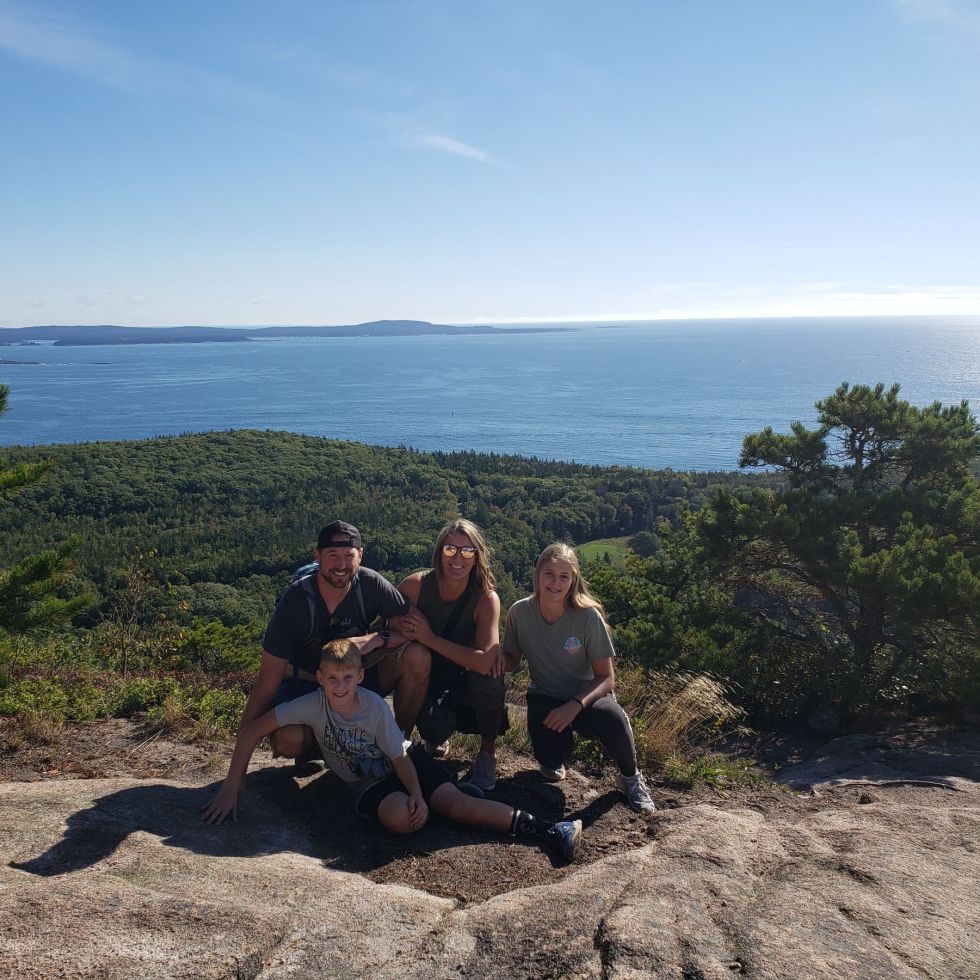 A family of 4 poses on a rock ground with the Atlantic Ocean behind them