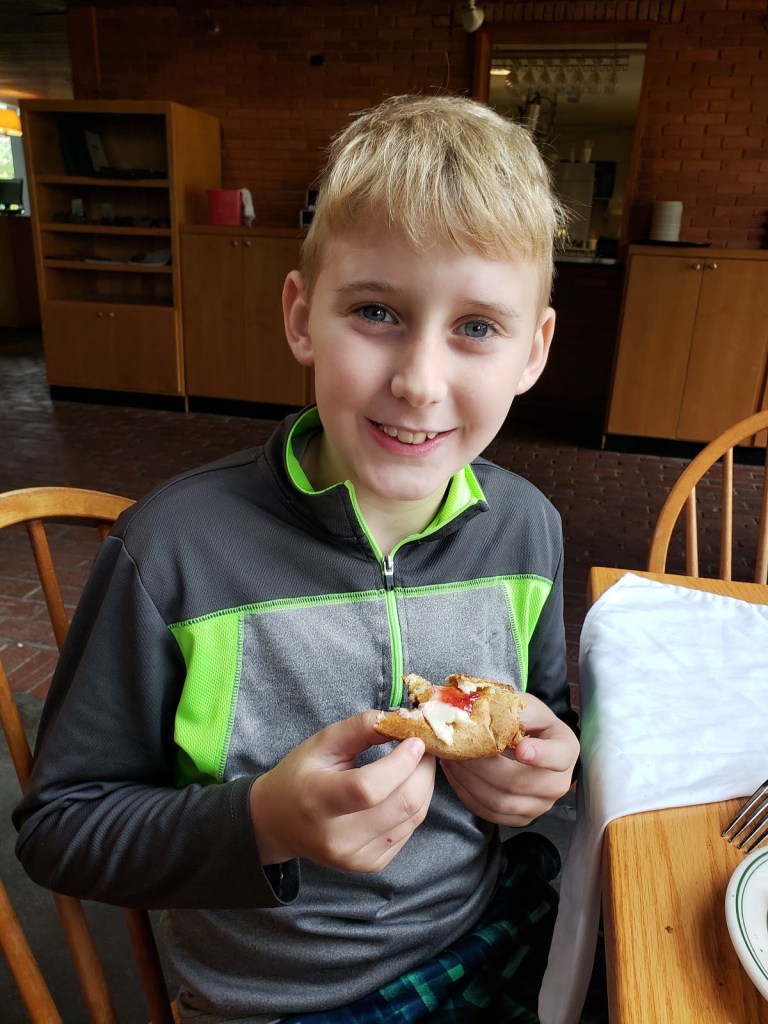 A boy smiles a toothy grin with a pastry with butter and red jelly