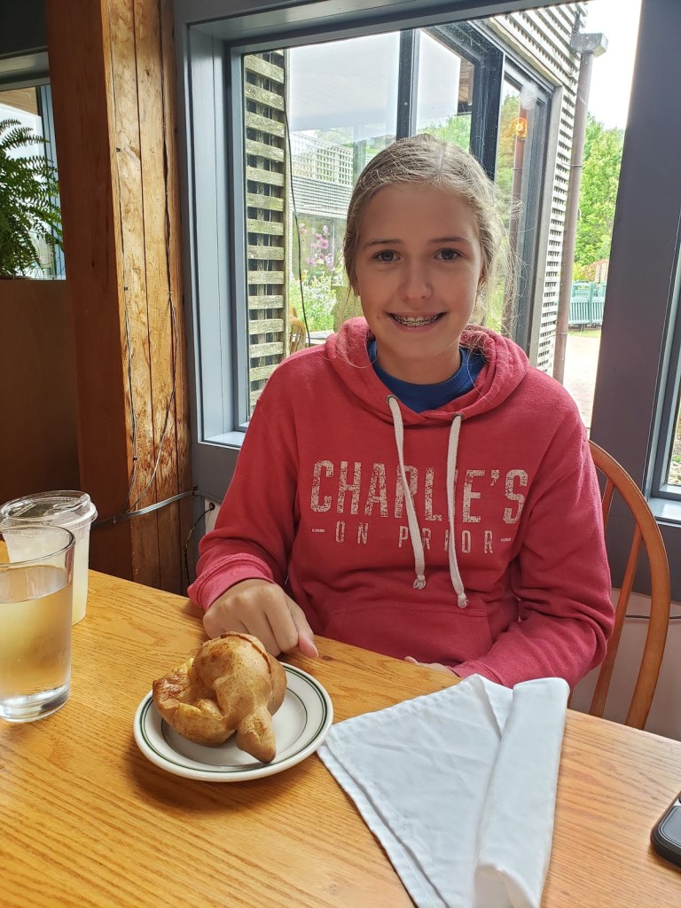 A girl with braces smiles in a red hooded sweatshirt behind an airy golden brown pastry