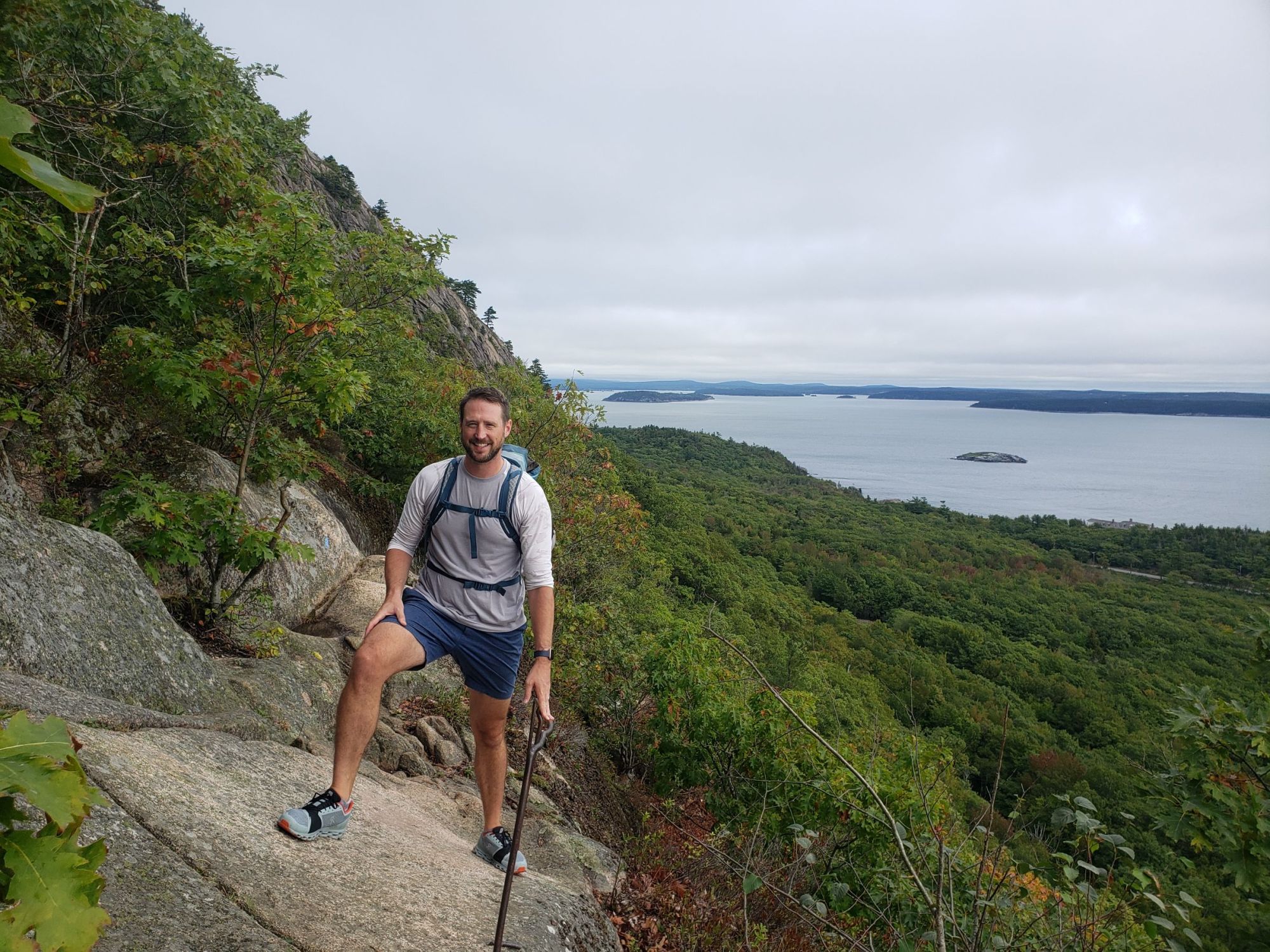 A man stands holding an iron railing on a bluff with islands peaking out of the ocean behind him