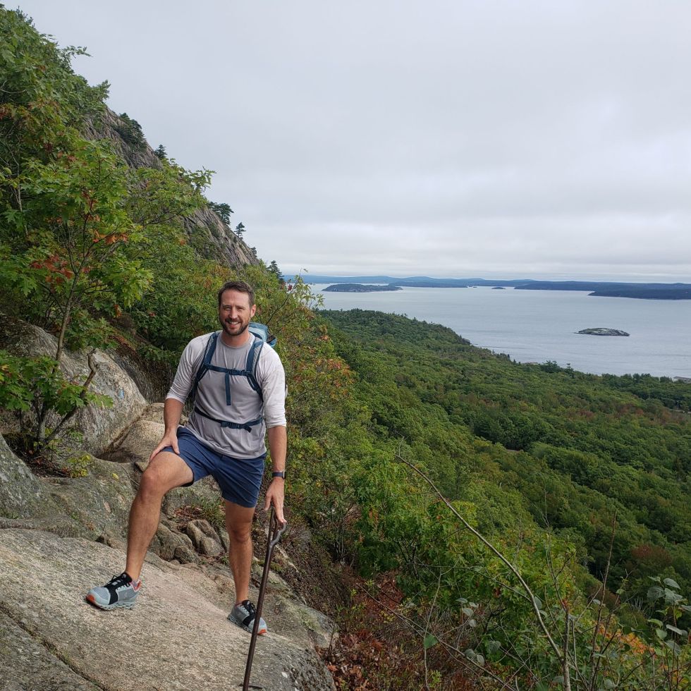 A man stands holding an iron railing on a bluff with islands peaking out of the ocean behind him