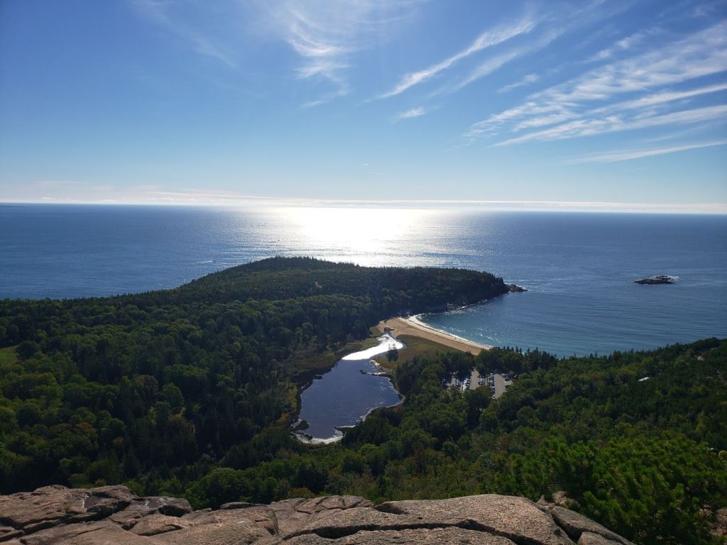 The sun reflects off the ocean with a sand beach dividing two bodies of water