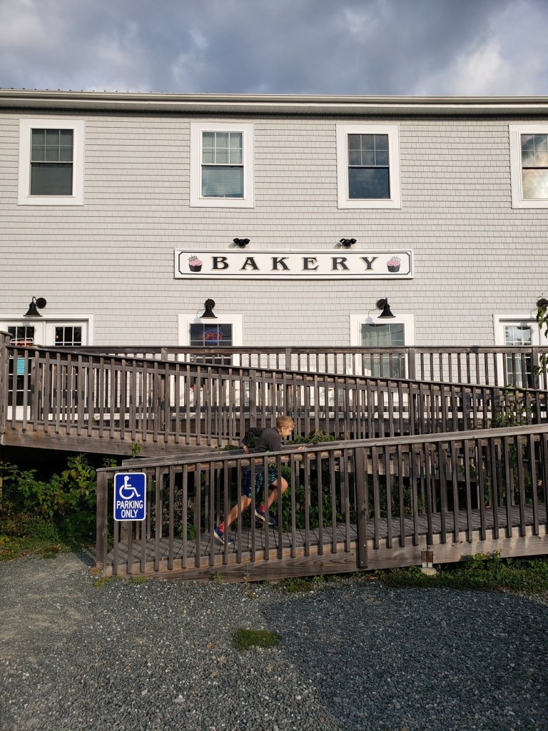 A boy running up a wooden wheelchair ramp in front of a bakery.