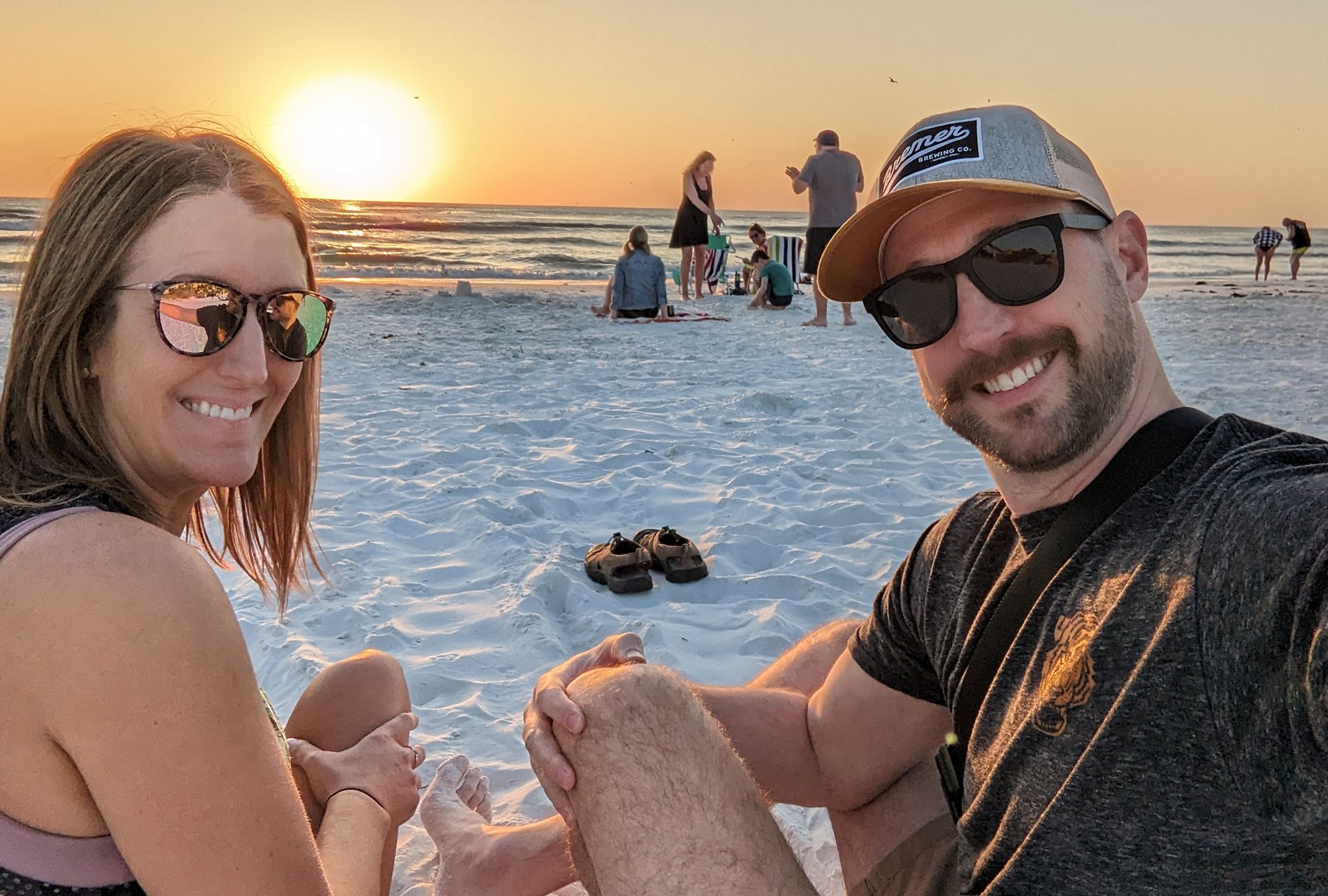 A couple smiling in front of a yellow sun over the ocean crashing against Crescent Beach
