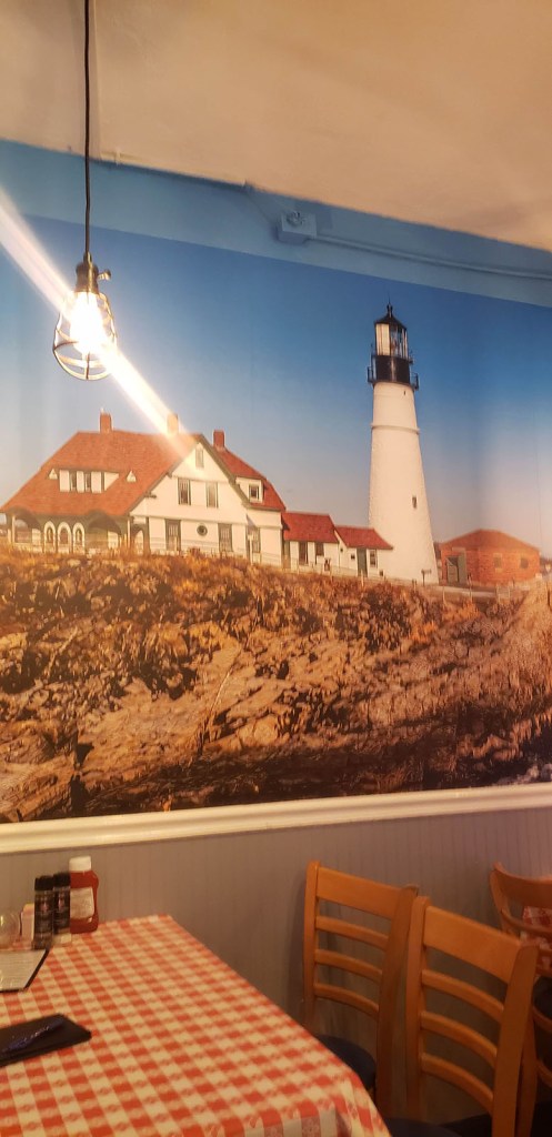 A large photo on the wall at a restaurant with a white lighthouse on the rocky coast
