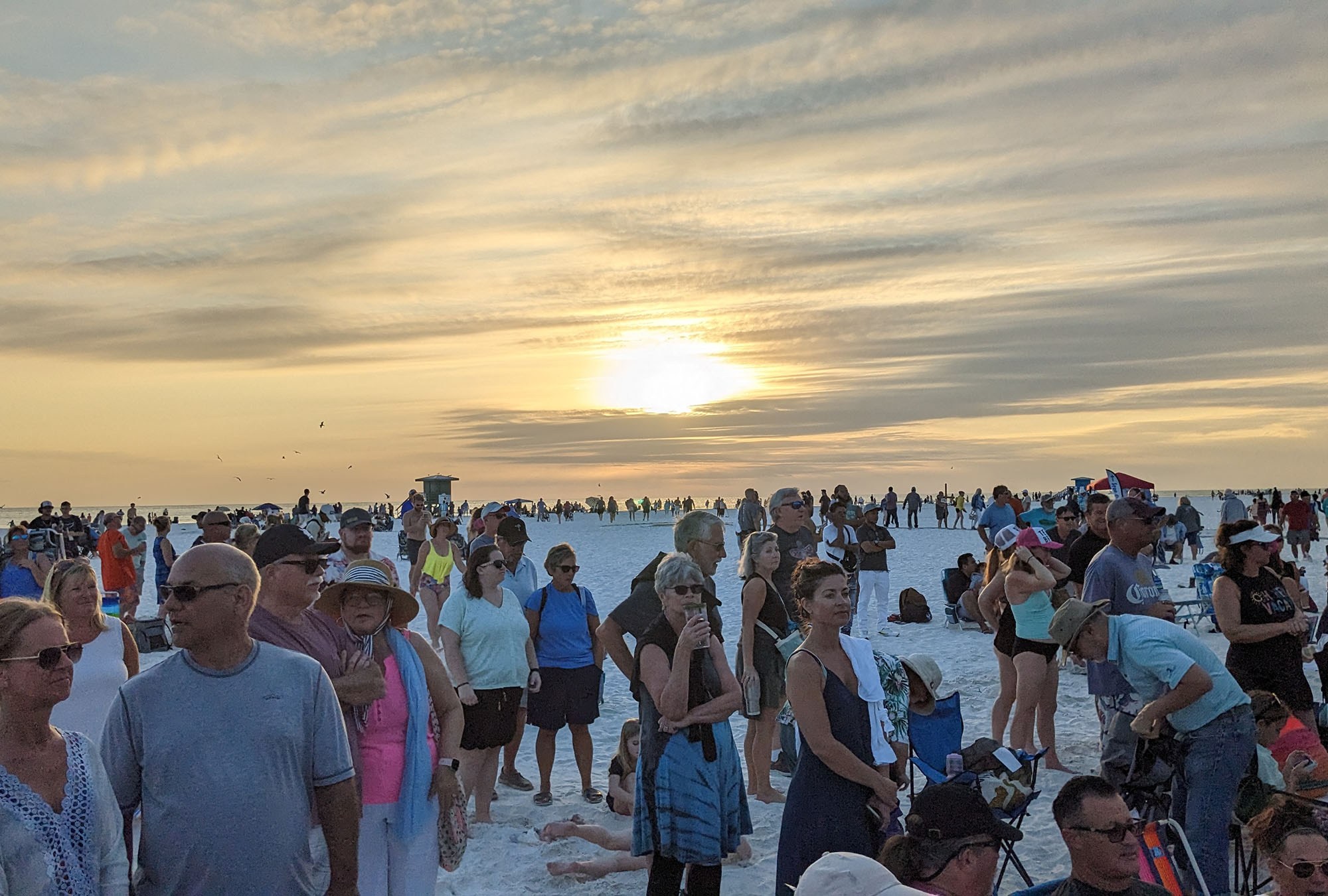 People watch and listen to a drum circle as the sun disappears behind the clouds.