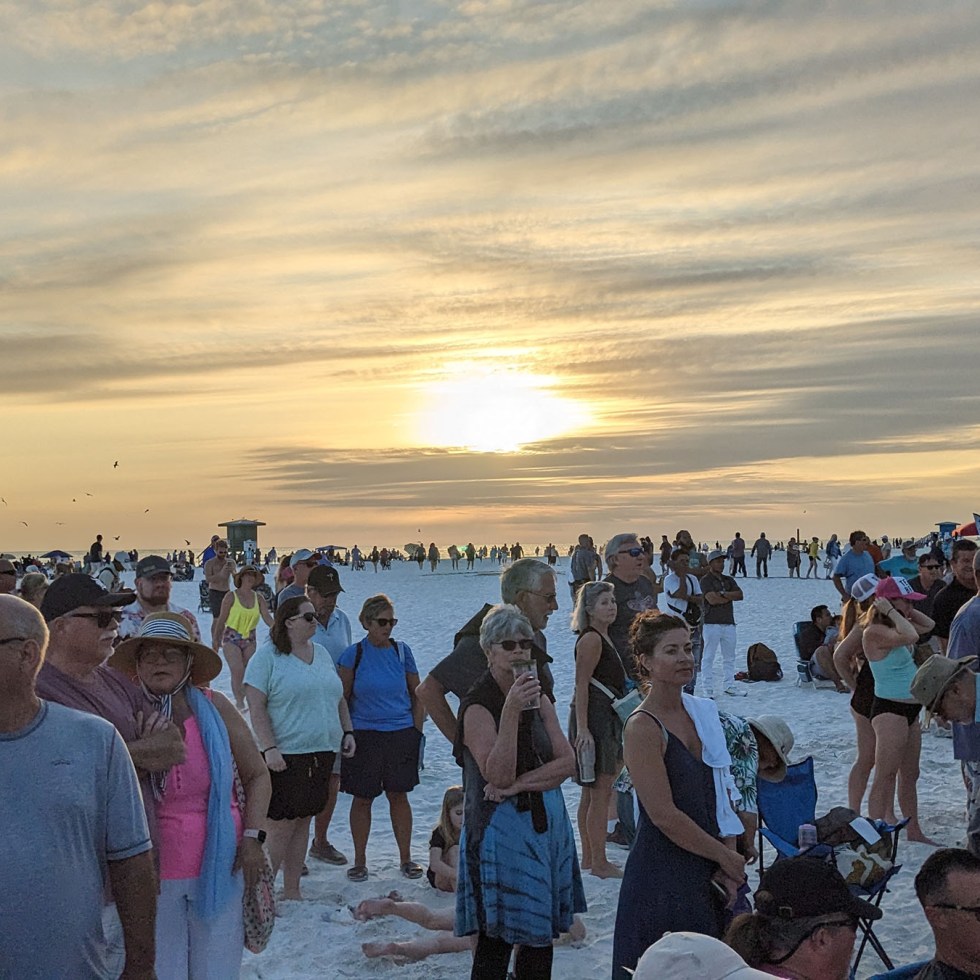 People watch and listen to a drum circle as the sun disappears behind the clouds.