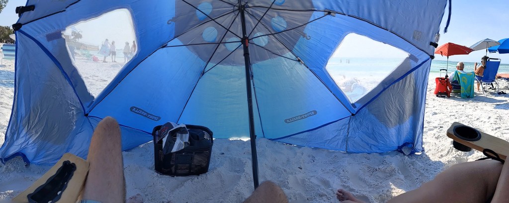 My umbrella fort that hid me from the sun. A blue umbrella in white sand.