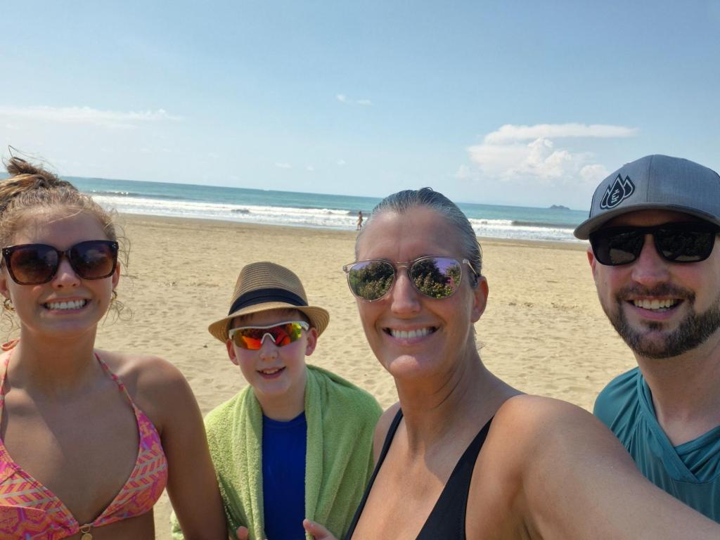 A family of four smiling with the beach and ocean in the background