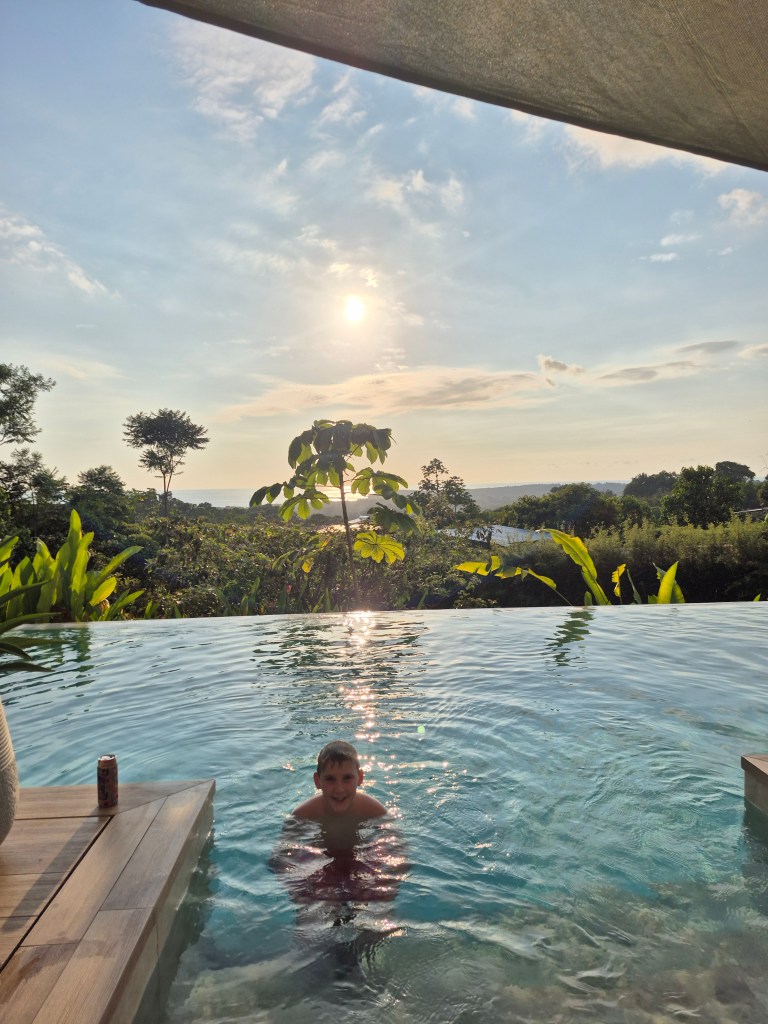 A boy with only his head out of the water in a pool overlooking the jungle and ocean in Costa Rica.