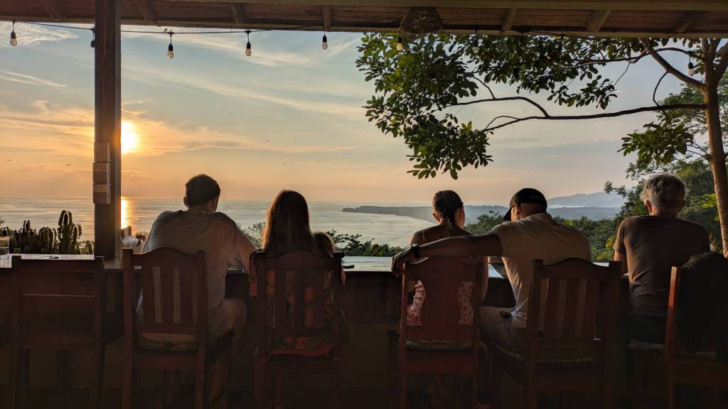The view from the bar seats from the restaurant. A group of 4 looks out over the ocean from their seats at a restaurant.
