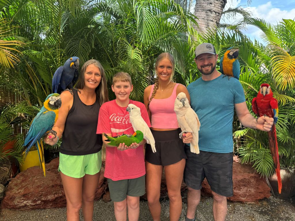 A family of four holds 7 colorful birds, smiling for a photo op.