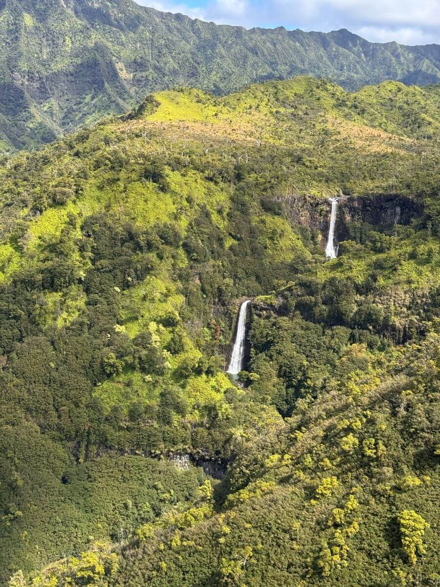One waterfall pours into another surrounded by green vegetation