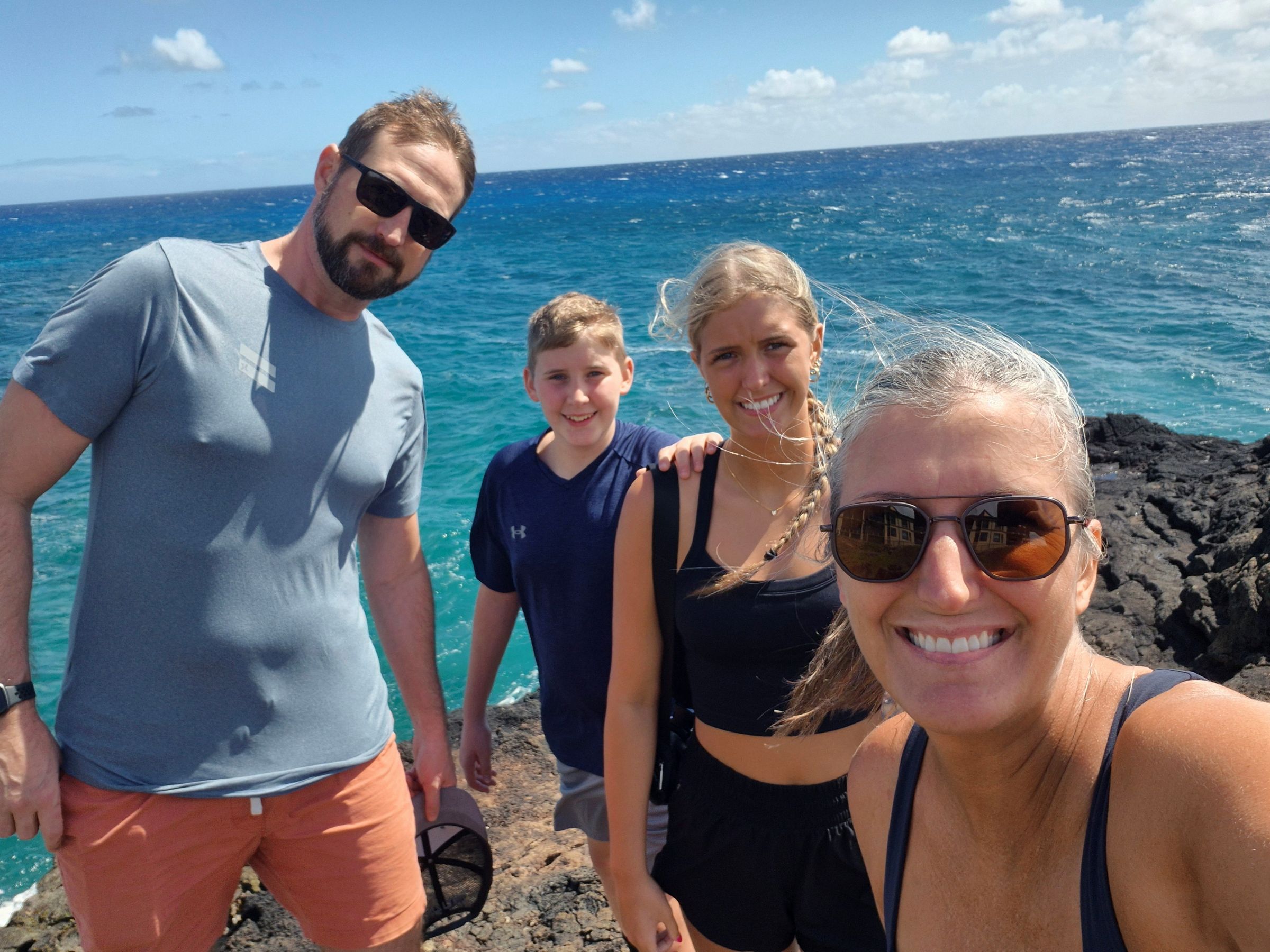 A family of four smiles at the camera with the ocean in the background.