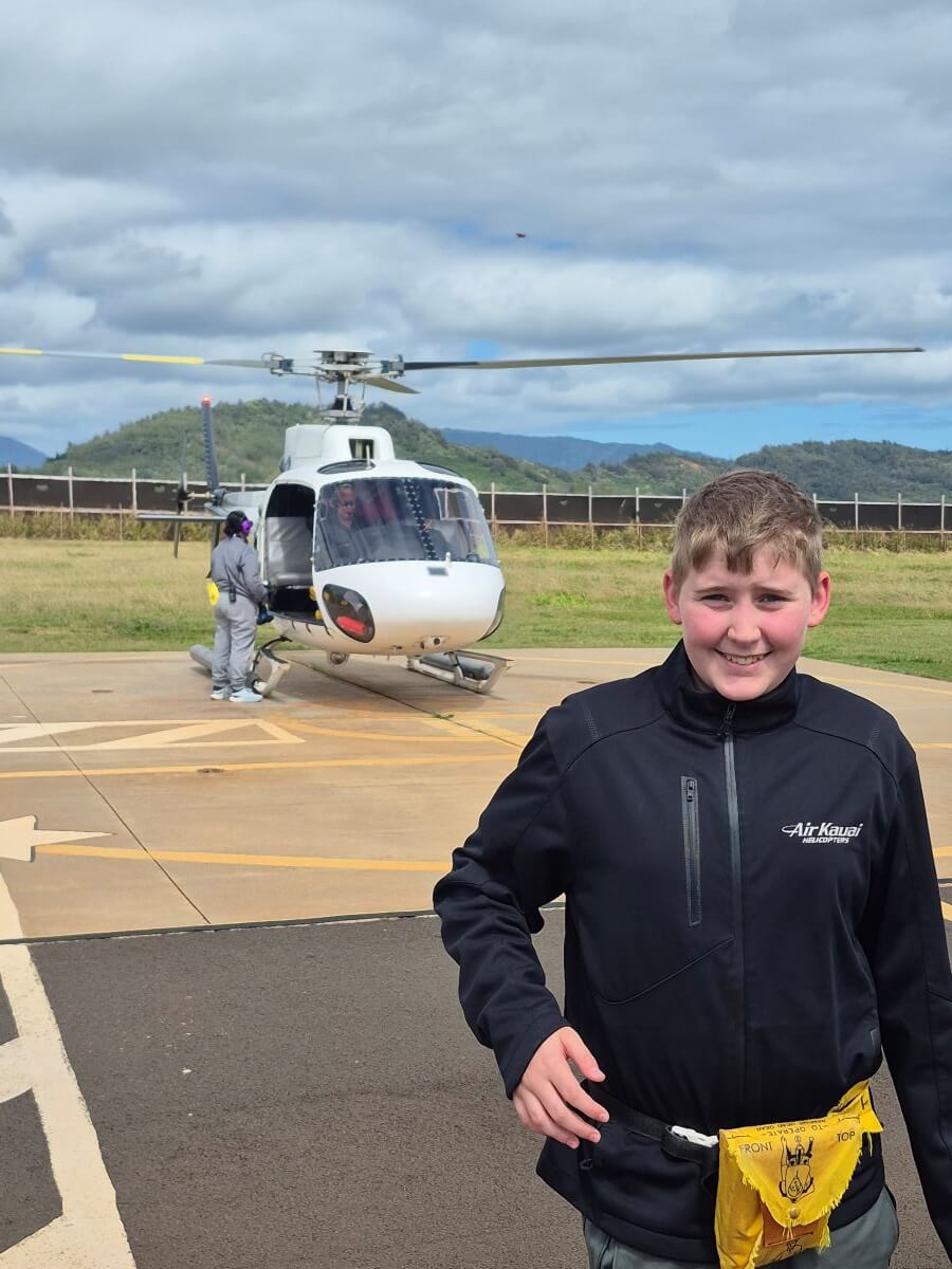 A boy smiling beside a helicopter