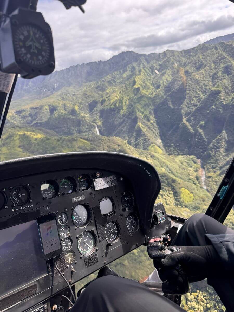 A view of the gauges of the helicopter with ridged green mountains showing through the window