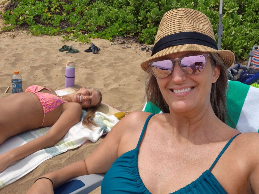 A mother and daughter smile at the camera while enjoying the sunshine at the beach.