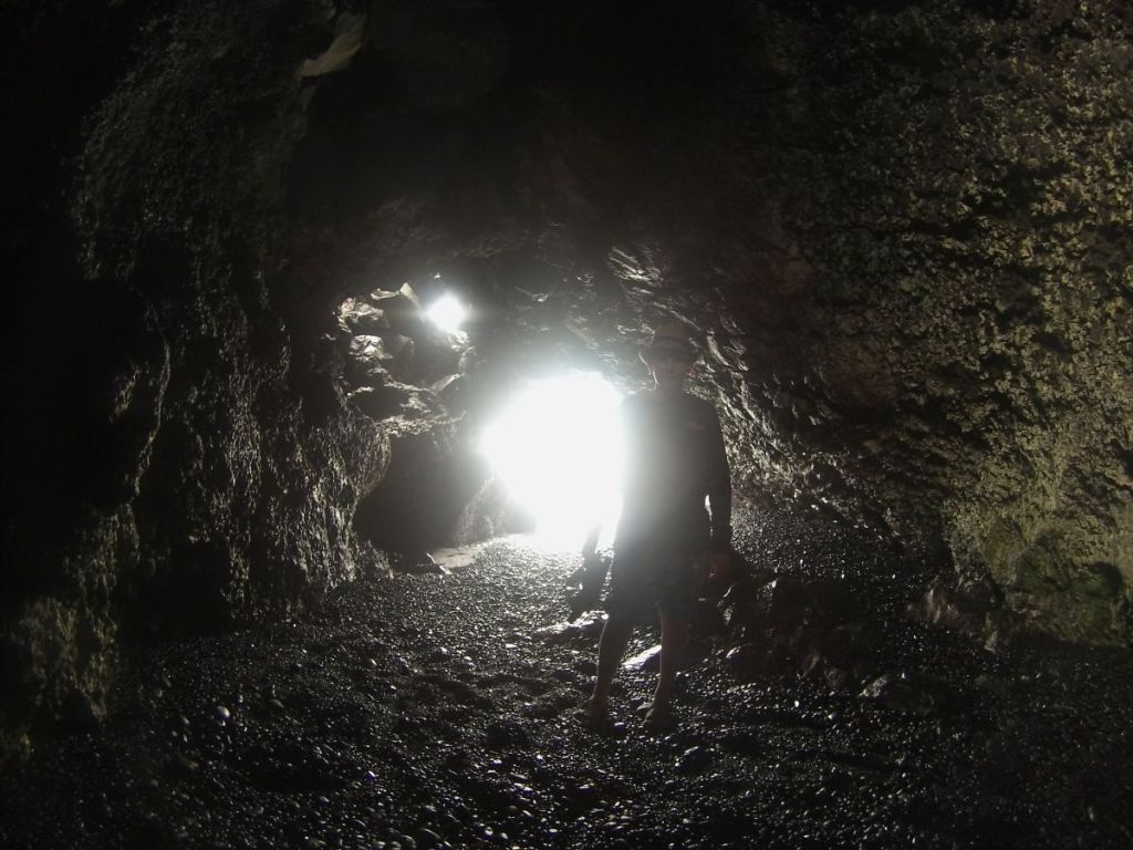 Mattix's silhouette against the bright light reflecting off the ocean water in a dark cave at Waianapanapa State Park