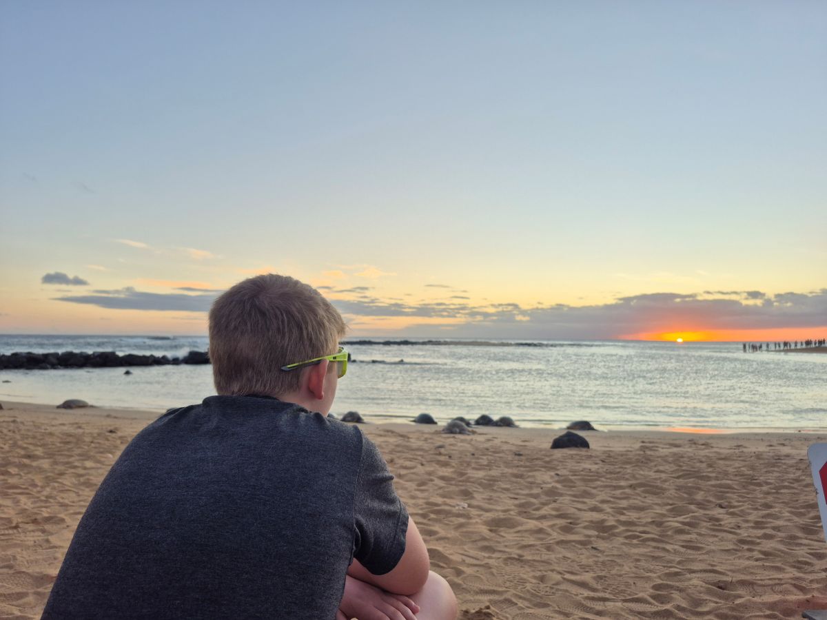 An adolescent boy admires the sunset over the ocean.