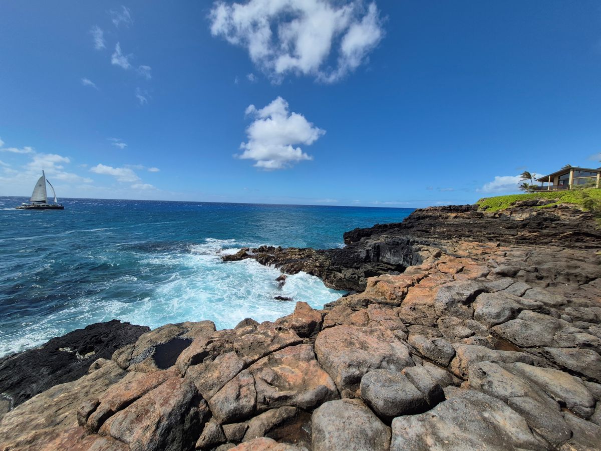 A bright blue sky fades into a dark blue ocean that foams as it crashes against the bluffs