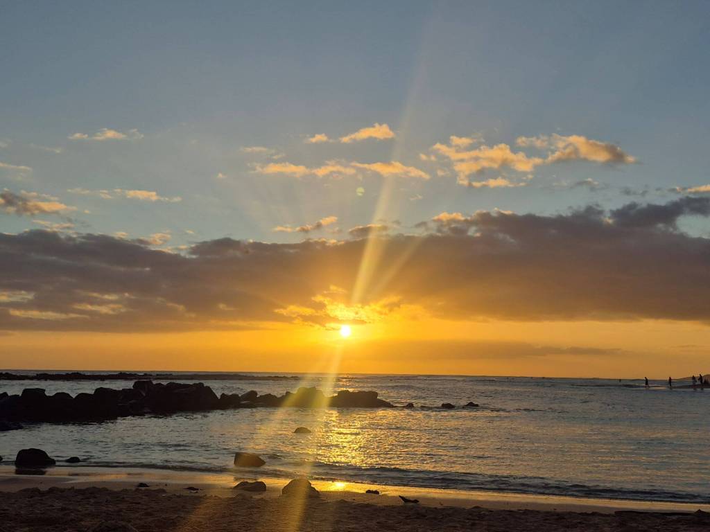 The sun's bright golden rays peek out from behind clouds over the Pacific ocean.