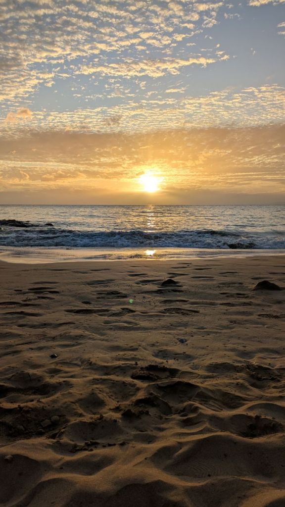 The sun peaking through the clouds over the ocean washing on a sandy beach