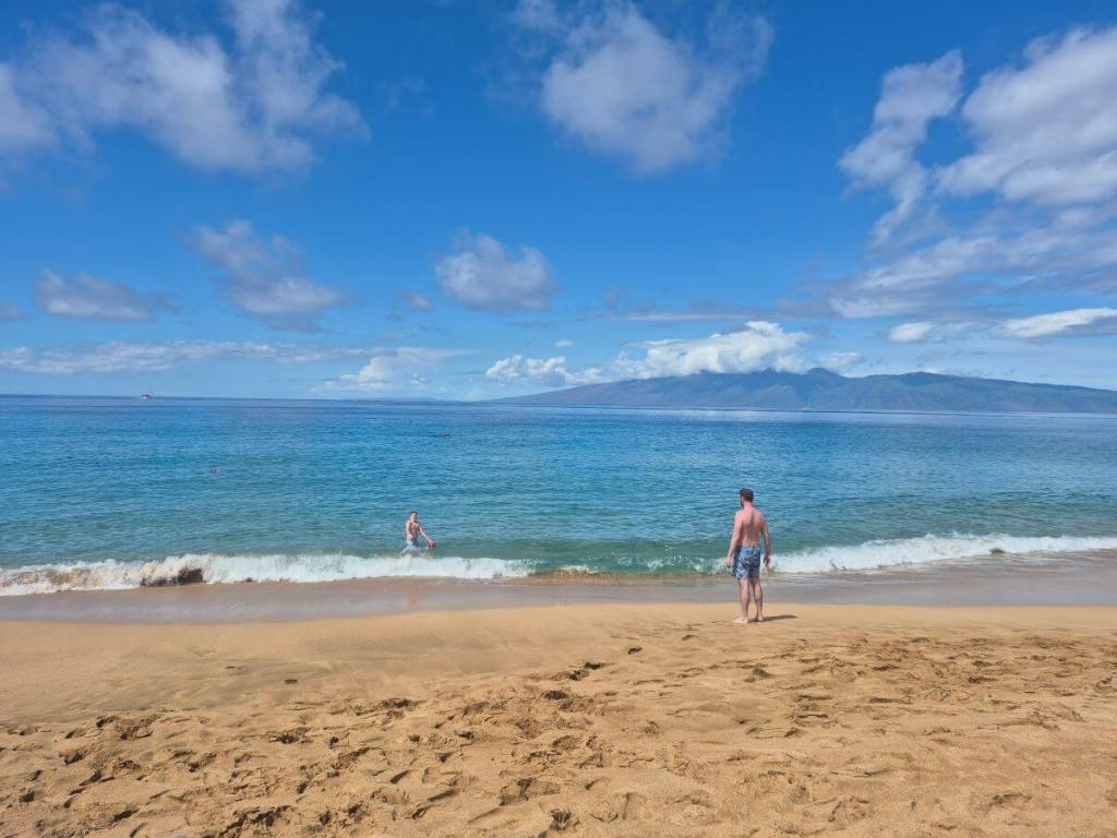 Playing catch with a football on the tan colored beach that has white waves washing up on the shore. The blue and water extends to the blue sky with an island in the distance.